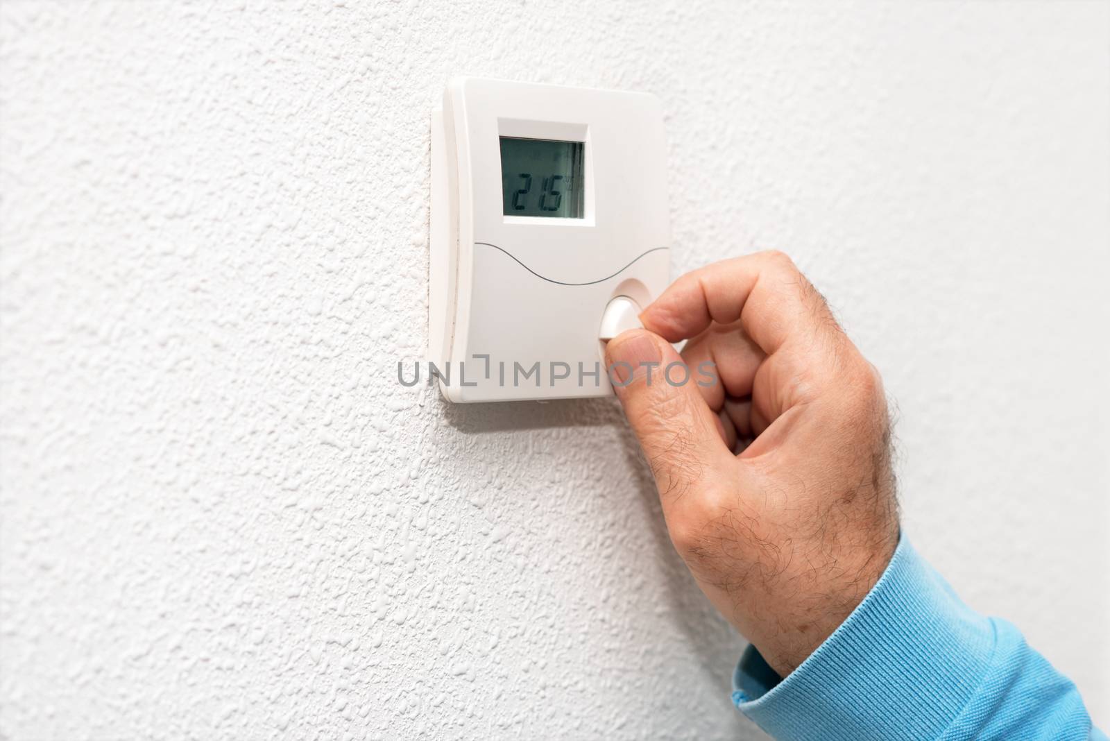 Man hand adjusting thermostat at home. Celsius temperature scale. by HERRAEZ