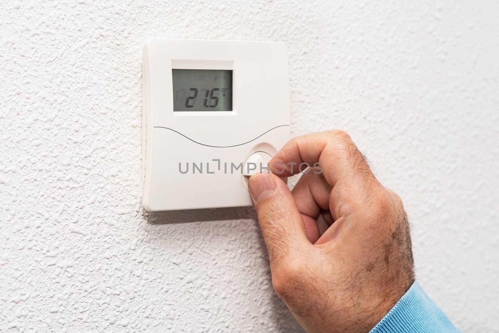 Man hand adjusting thermostat at home. Celsius temperature scale.