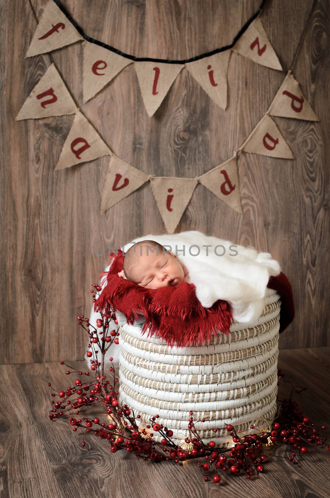 Lovely baby sleeping on a basket with brown, wooden background and Merry Christmas letters.