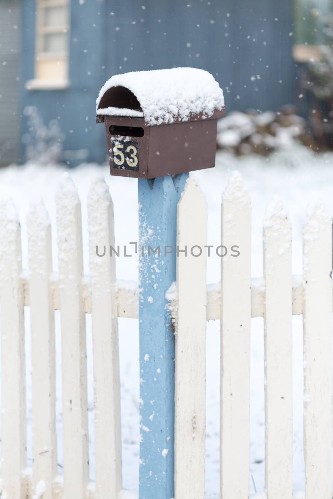 Snow covered picket fence and mail box with light falling snow in winter