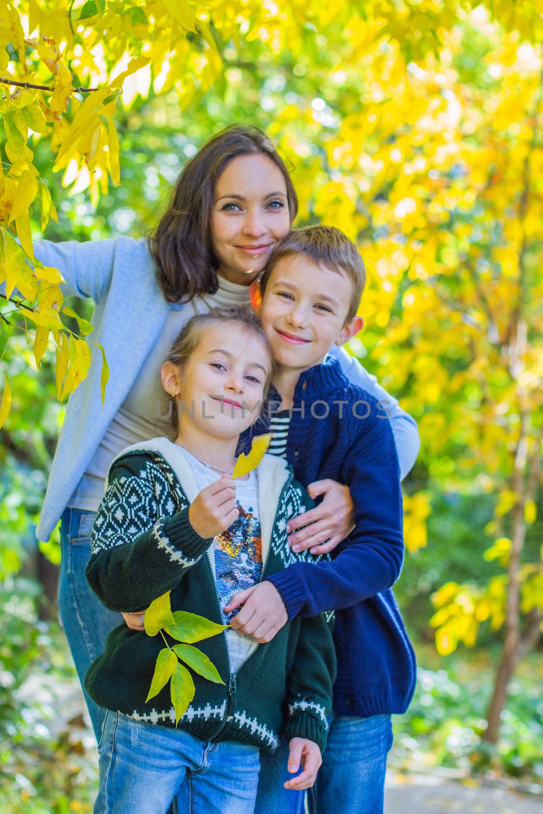 Mother with two children under autumn yellow tree smiling by Angel_a