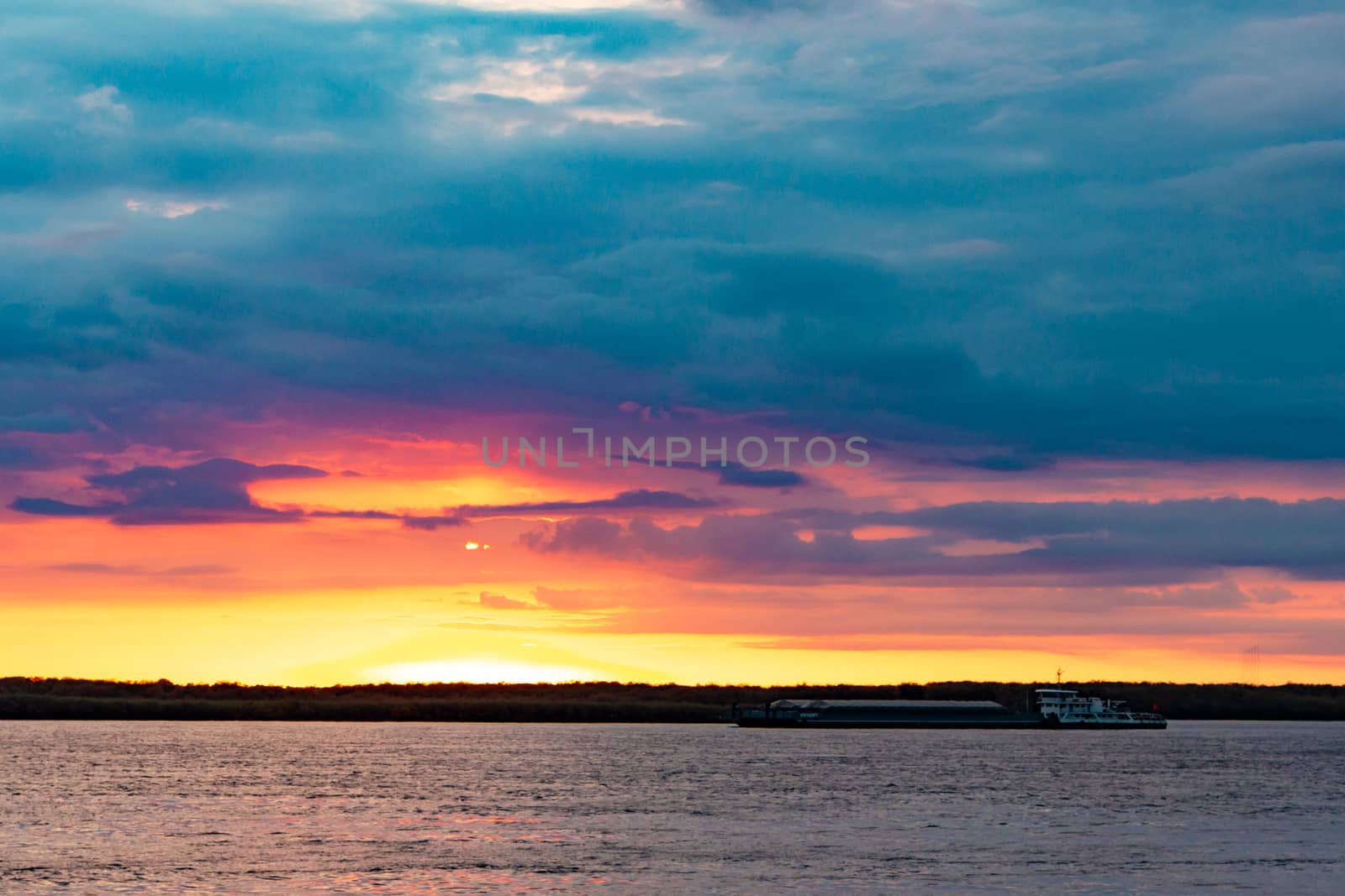 Sunset on the embankment of the Amur river in Khabarovsk. The sun set over the horizon. The embankment is lit by lanterns. People walk along the river Bank.