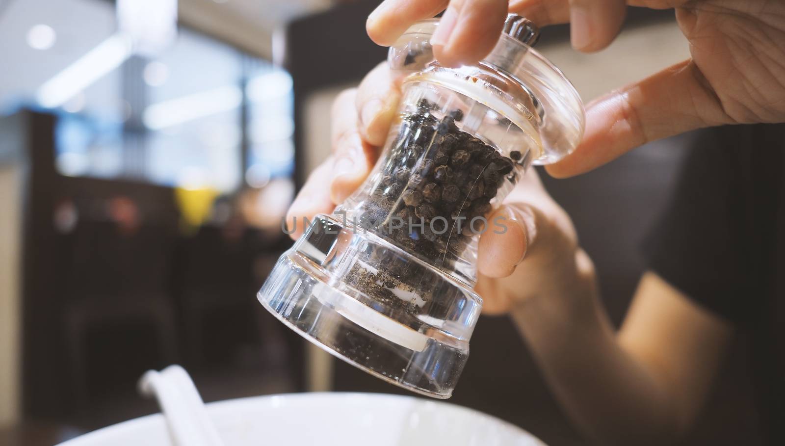 Clear color glass and Thailand black pepper mill or grinder in hands that twisting the bottle and pouring or adding small pieces of spices to plate or bowl for a better taste in the meal.