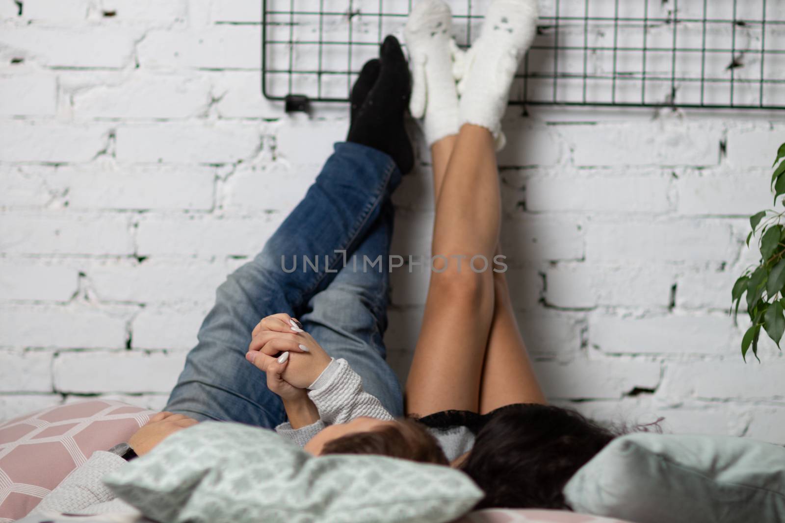A young man and his girlfriend lying on the bed, throwing his feet on the wall of white brick by rdv27