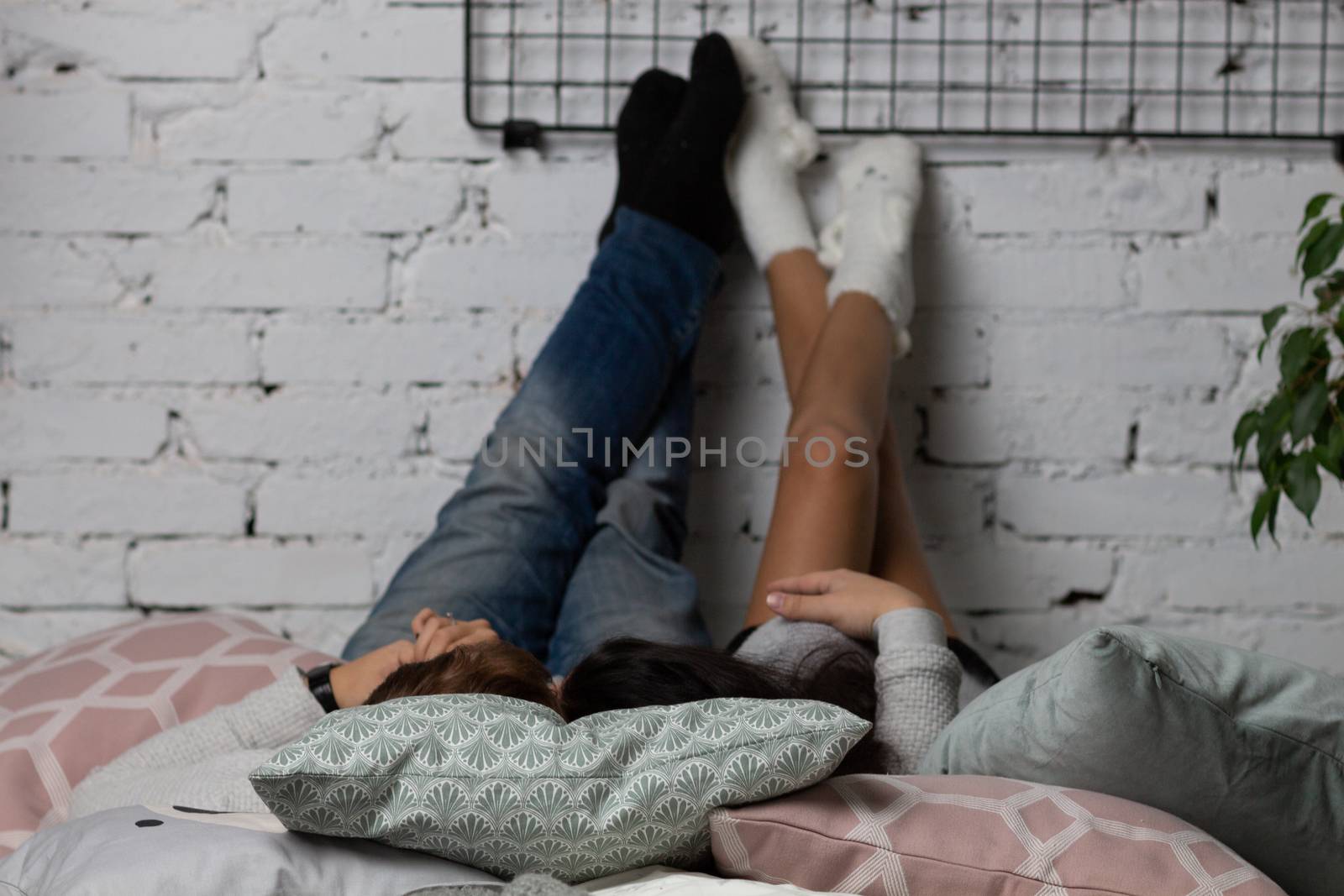 Girl and guy lay back on the bed and his feet on the wall of white brick.