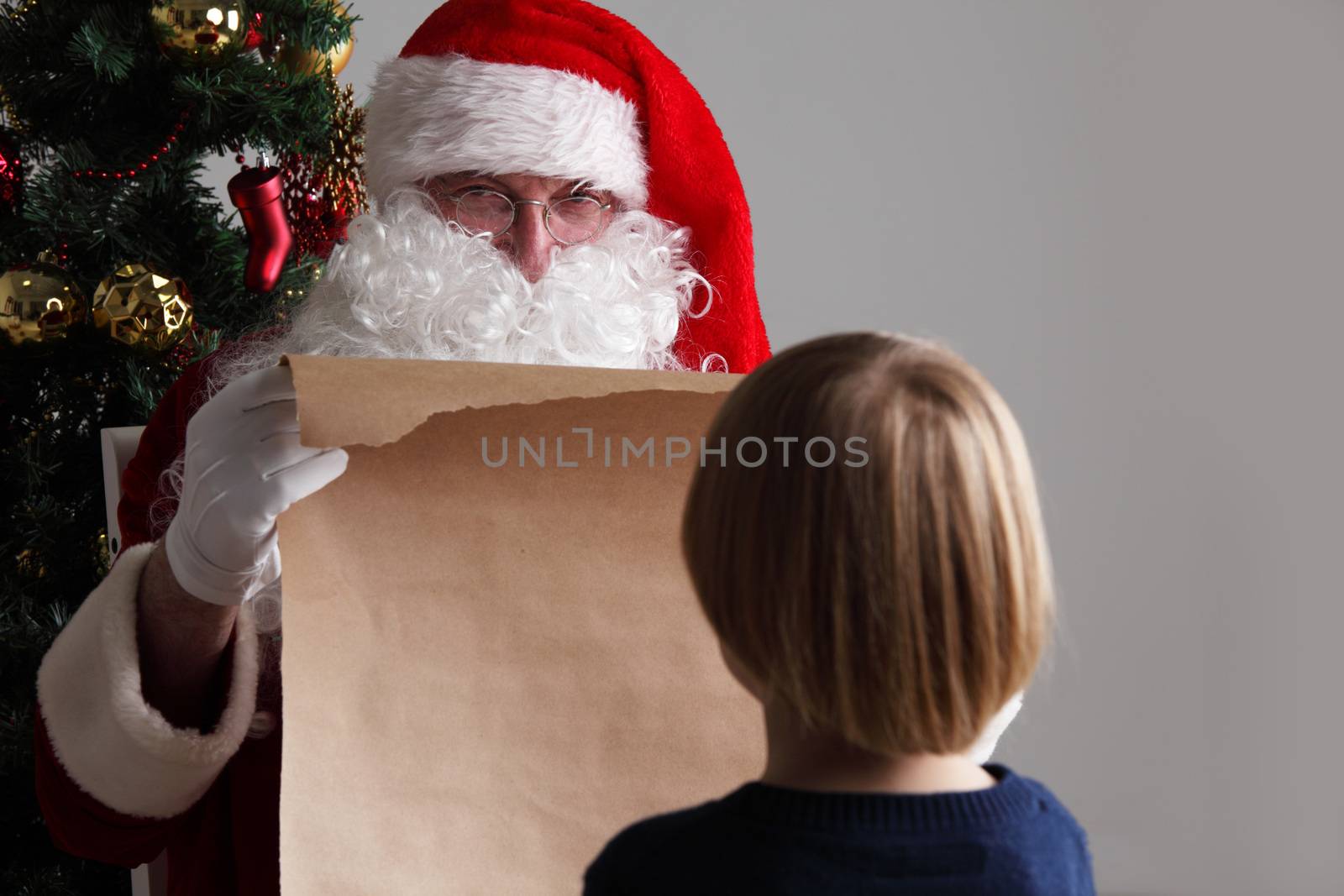 Santa Claus with with list or nice or naugthy list paper with small boy near christmas tree