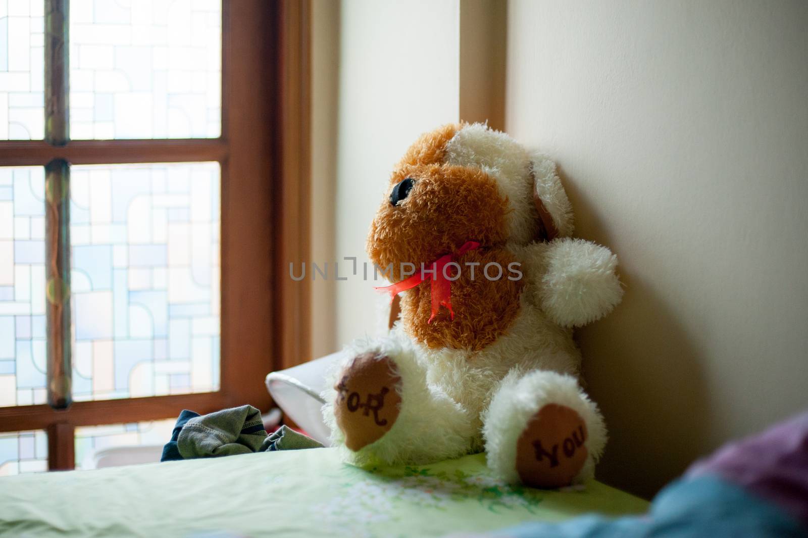 Stuffy animal of dog is on the bed. This doll is a present from your lovable person.
