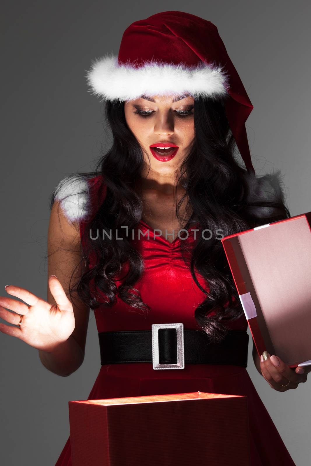 Beautiful woman in Santa Claus style costume looking into glowing Christmas gift box
