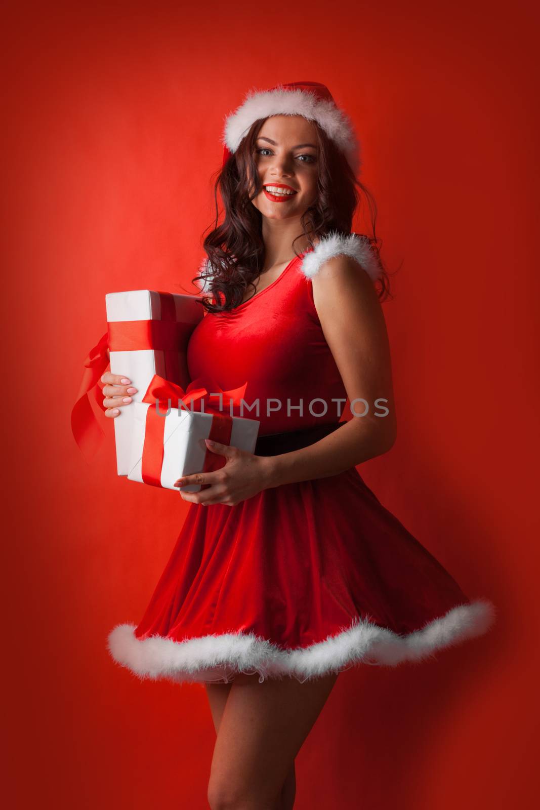 Beautiful young woman in Santa dress and hat celebrating Christmas holding gift boxes