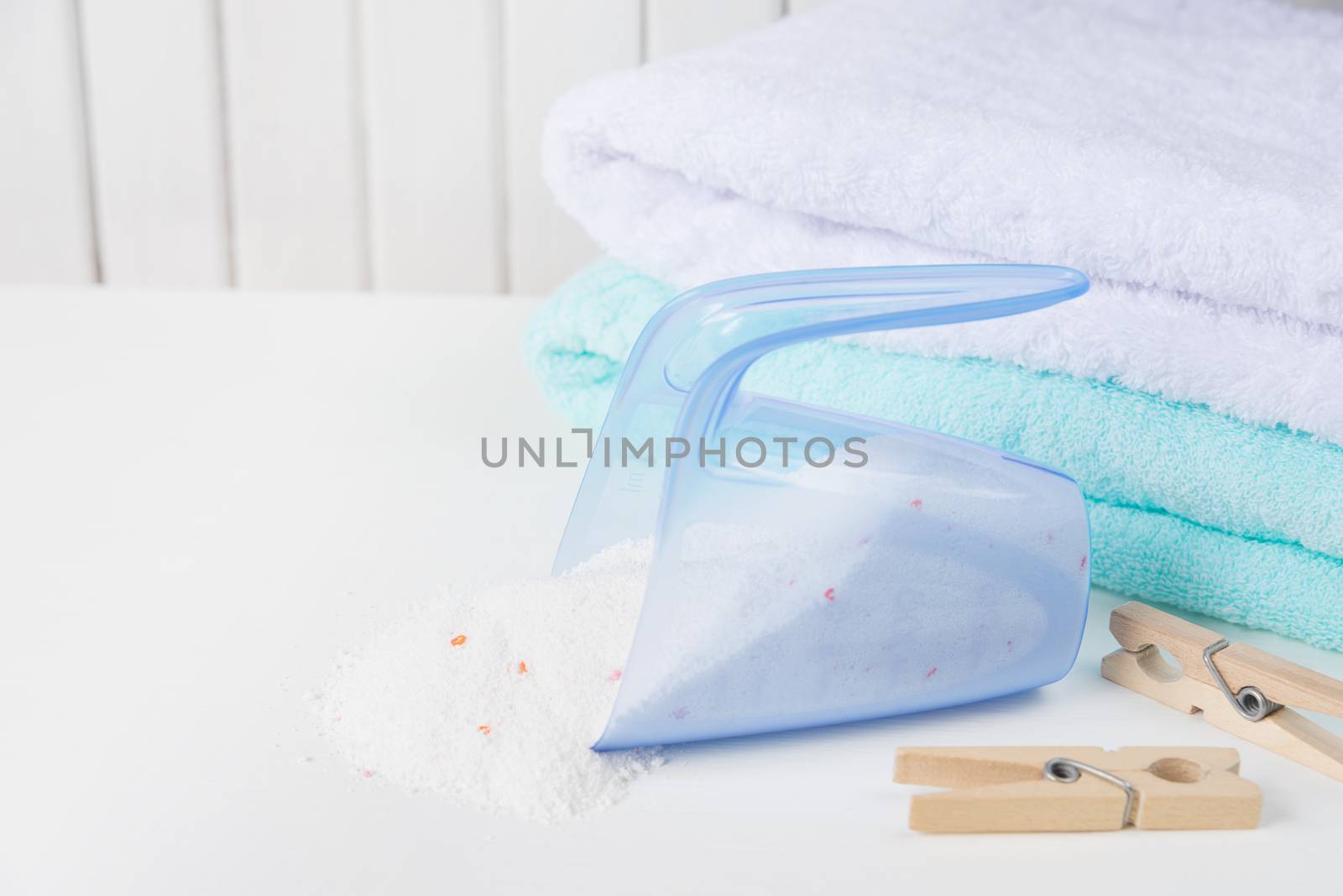 Stack of white and blue fluffy bath towels, washing powder spilled from a measuring cup and wooden clothespins on the background of white boards
