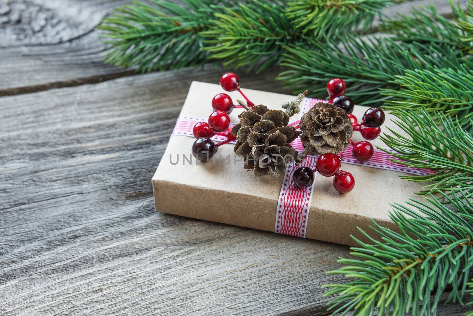 Christmas composition of pine cones, spruce branches and gift box with fir cones and holly berries on the background of old unpainted wooden boards; with copy-space