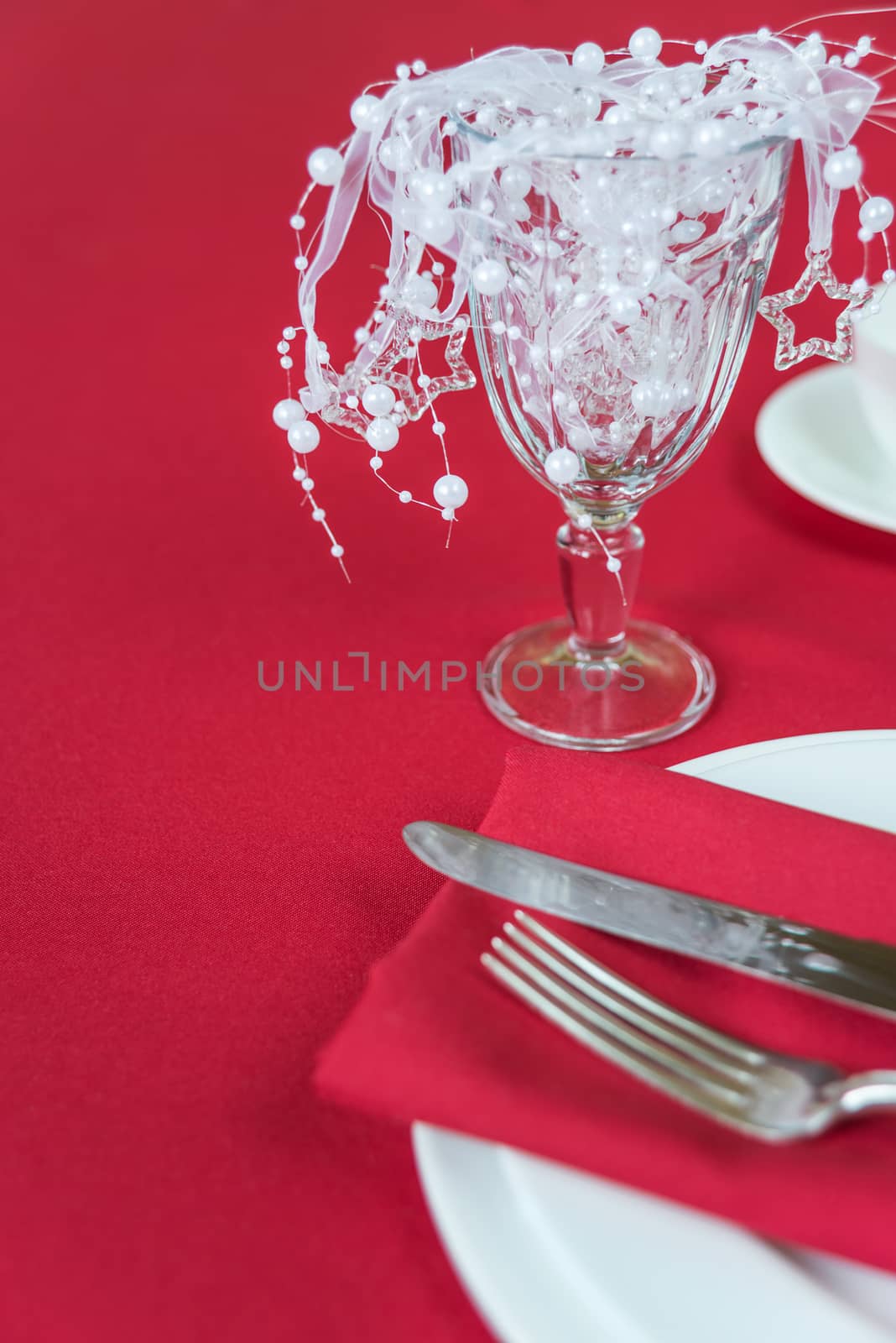 Silver knife and fork lie on the red linen napkin, as well as wineglass, which is located on a table covered with a red tablecloth, with space for text