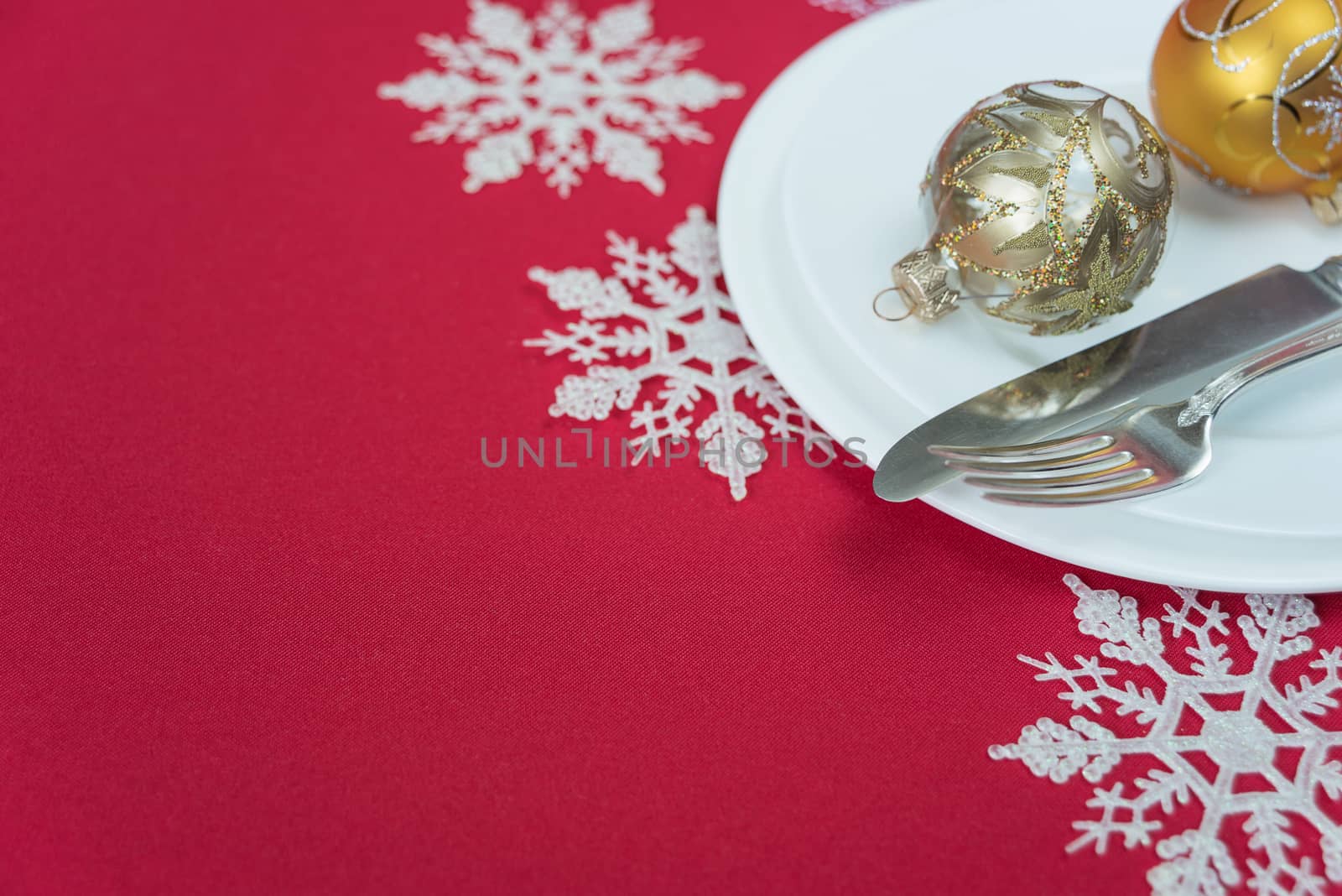 Christmas table: silver knife and fork, beautiful Christmas ball are on the white porcelain plate, which is located on a table covered with a red tablecloth; with space for text