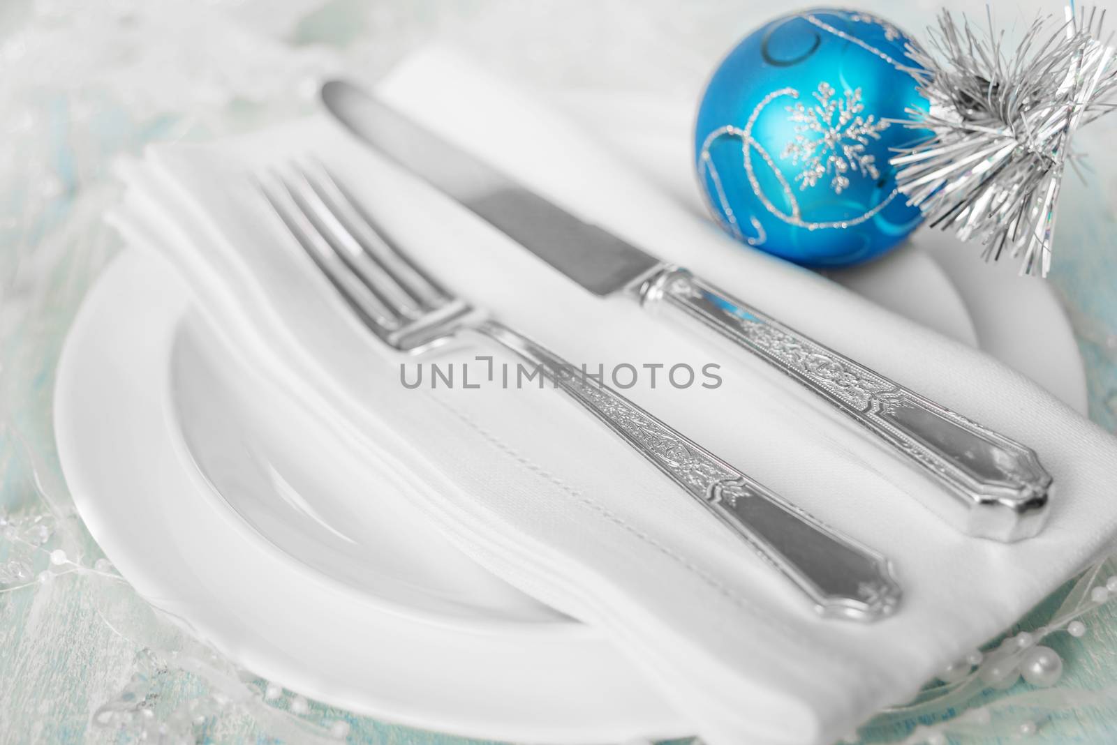 Christmas table with white plates, linen napkin, silver knife and fork and a beautiful blue Christmas ball