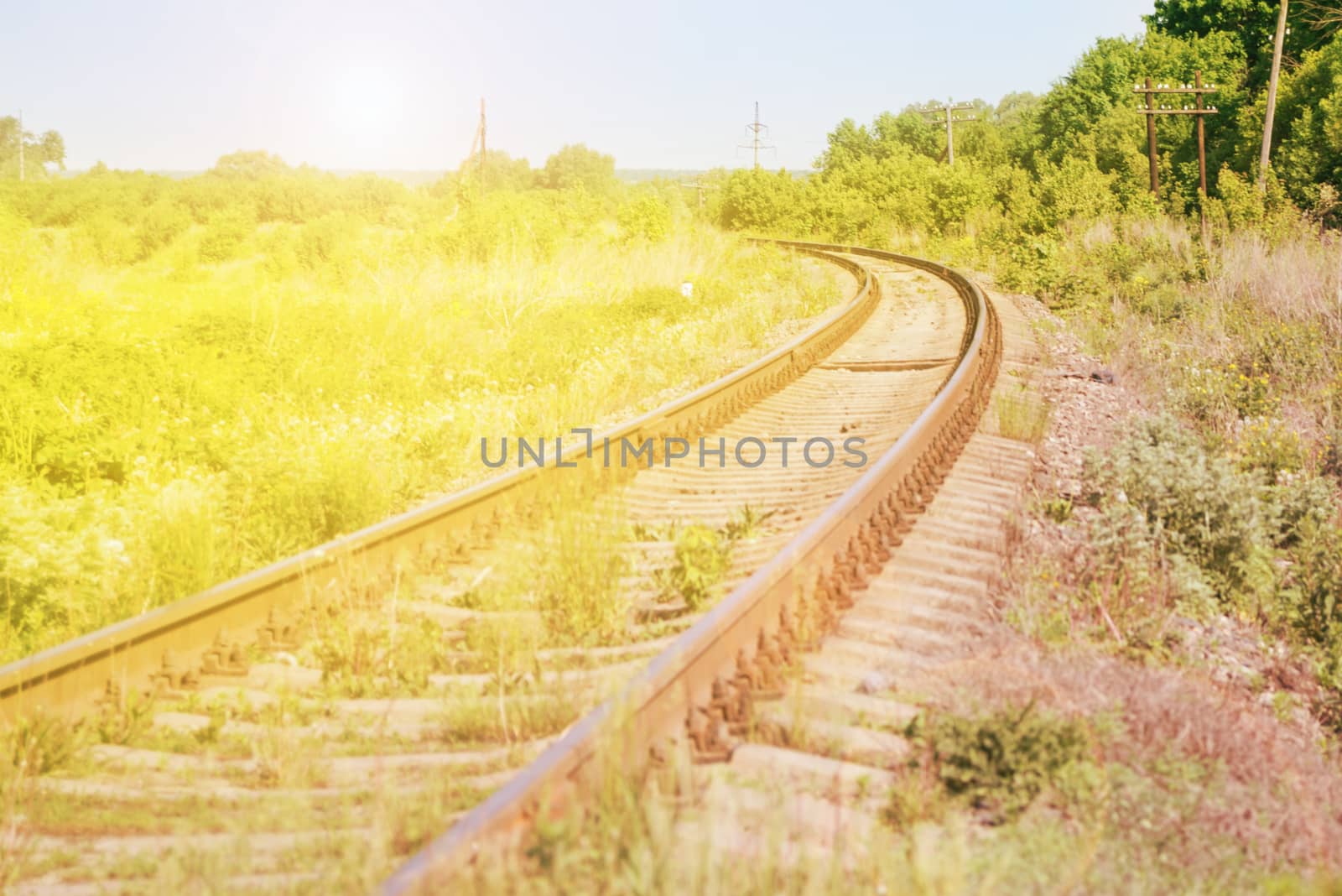 Railroad against beautiful sky at sunset. Industrial landscape with a railway, colorful blue sky, trees and grass, yellow sunlight. Cargo shipping concept.