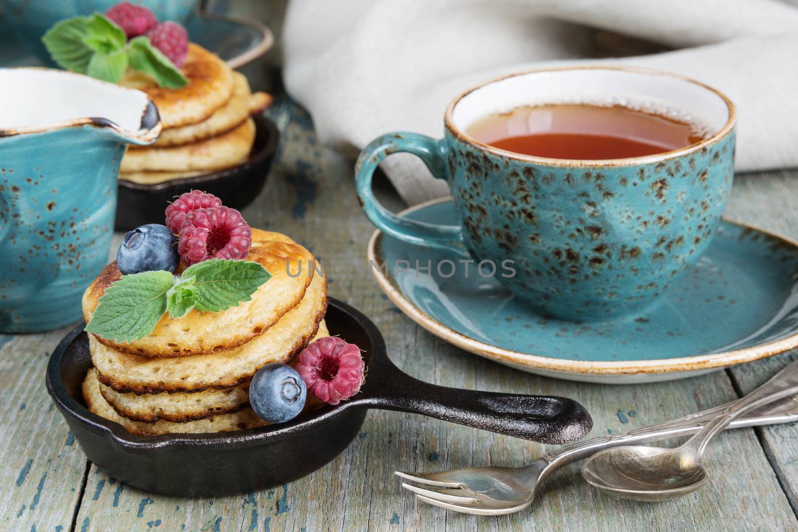 Breakfast of pancakes, fresh berries and black tea in blue ceramic cup in rustic style
