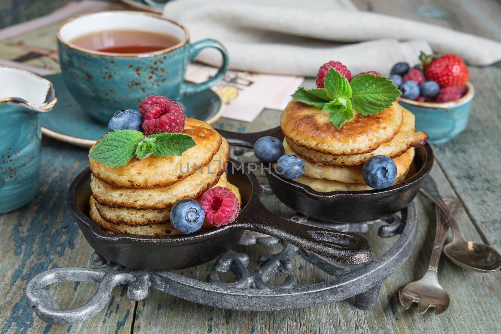 Breakfast of pancakes, fresh raspberries, blueberries and black tea in blue ceramic vintage cup, in rustic style