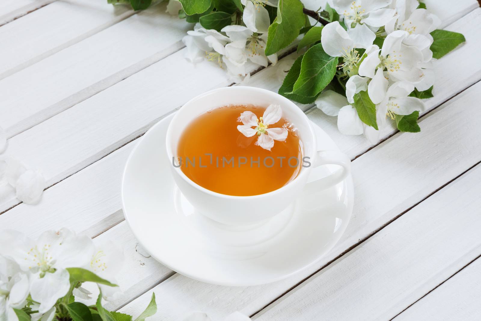 White porcelain cup cup of green tea and branches of apple-tree flowers on an old white wooden shabby background