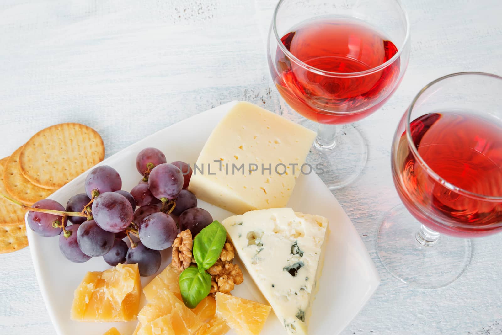 Two glasses of red wine, different varieties of cheese, walnuts, red grapes and basil leaves, top view