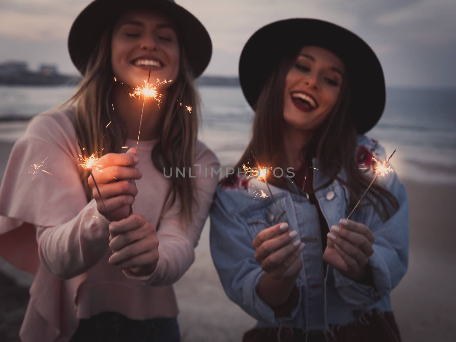 Two beautiful friends celebrating holding sparklers at beach 