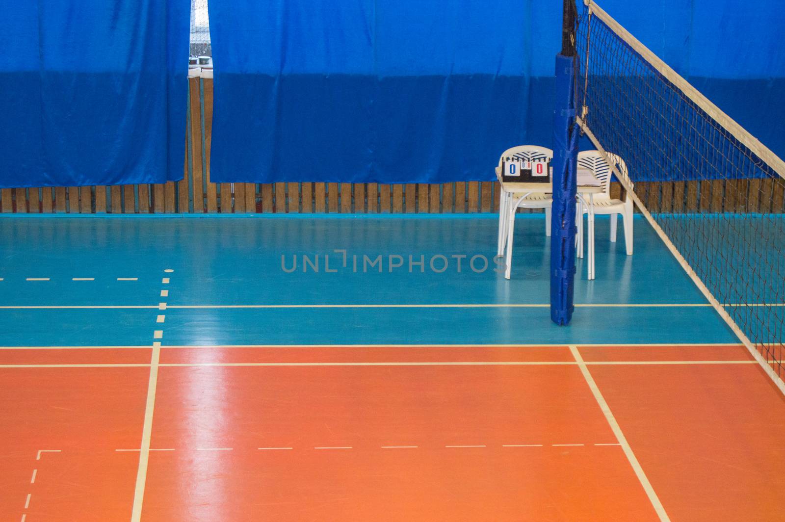 An empty gym with a volleyball net, chairs and display Board in the school.