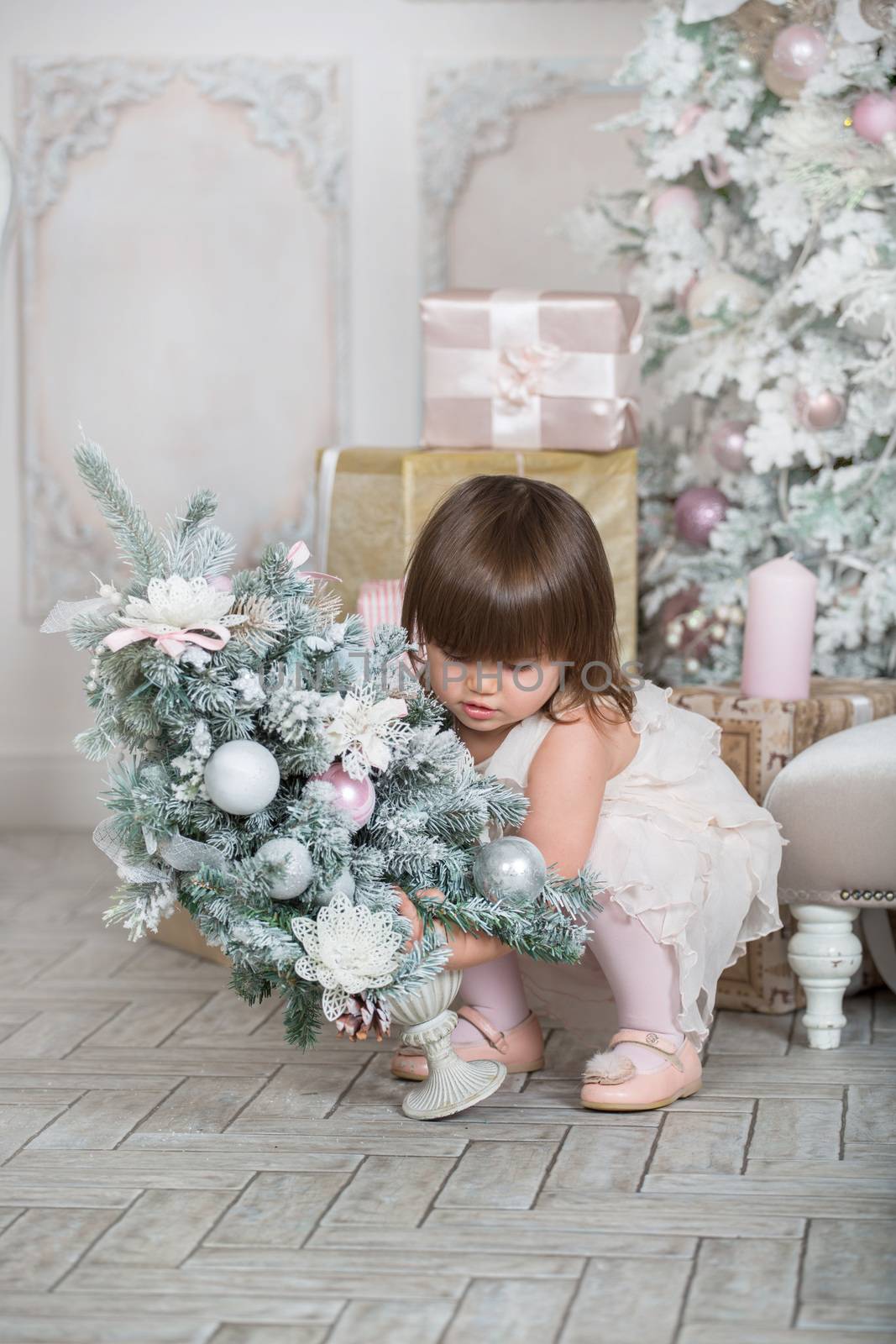 Merry Christmas and Happy Holidays! Cute funny little child girl is decorating the Christmas tree indoors