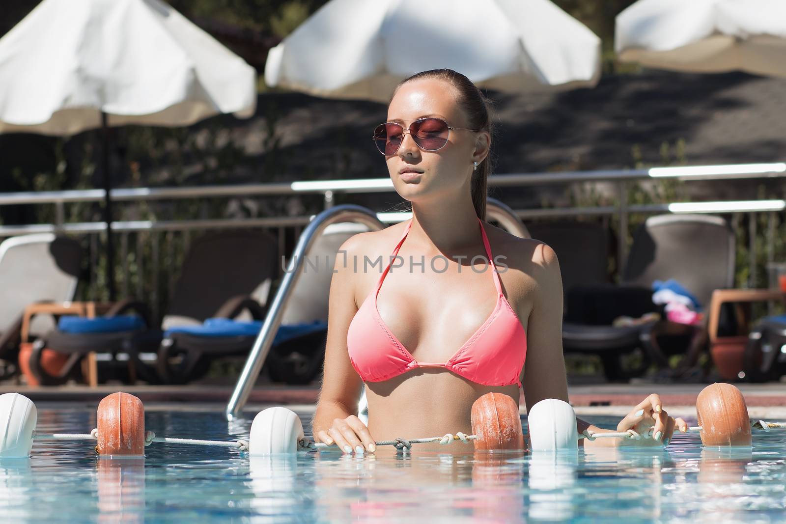 From below shot of sensual wet female in swimwear climbing up ladder of swimming pool on sunny day