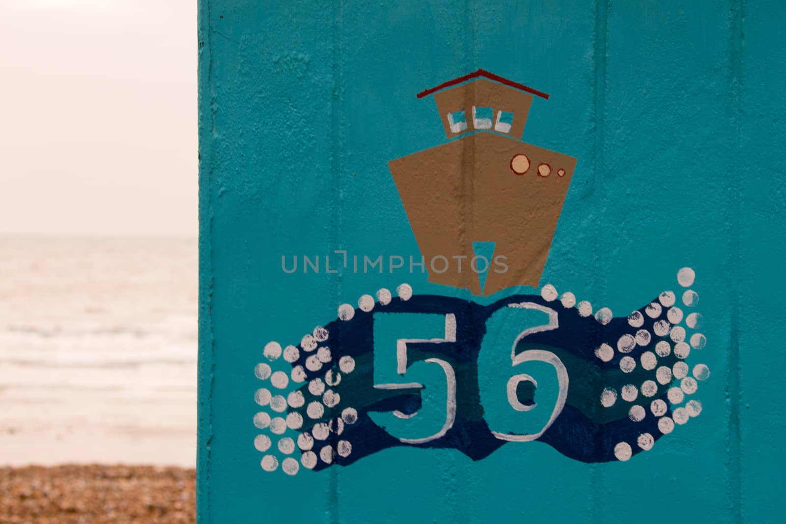 Brown painted boat on on a blue english beach hut with the number 56 and the beach and sea in the background