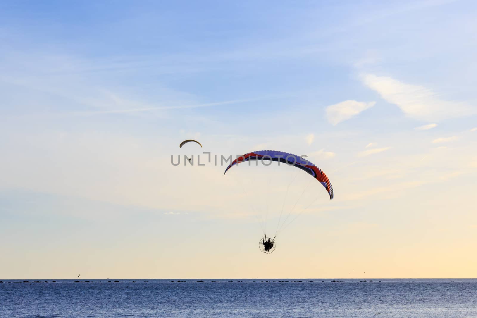 2 powered paragliders with red and blue canopies above a blue sea and soft clouds