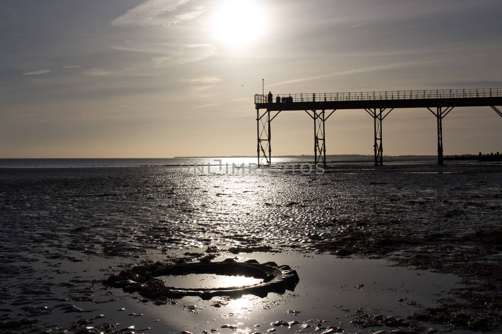 low tide warm sunset, man stood on old english victorian pier with tractor tyre in foreground