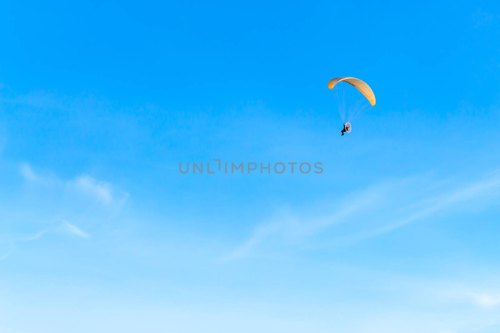 Single Powered paraglider with red and yellow canopy in blue sky and soft wispy clouds