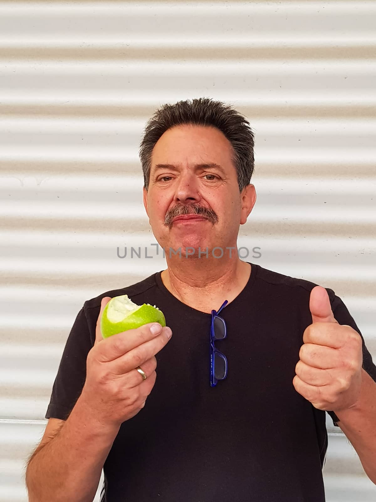 Portrait of a man in front of light background is eating a green sour apple and grimacing.