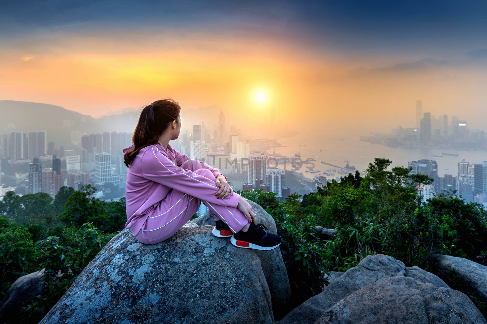 Woman sitting on the rock and looking to Hong Kong at sunset.