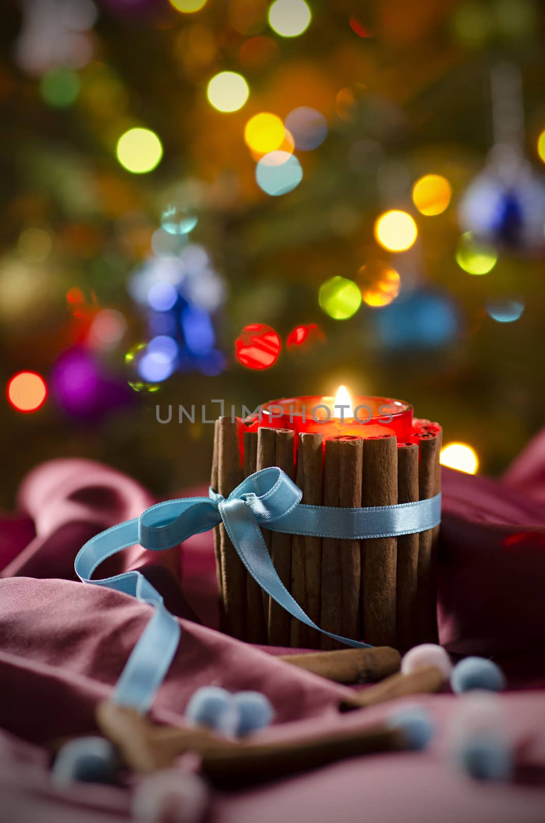 Christmas candle on the background of branches of  Christmas tree and luminous garlands. Burning candle in front of Christmas Tree.