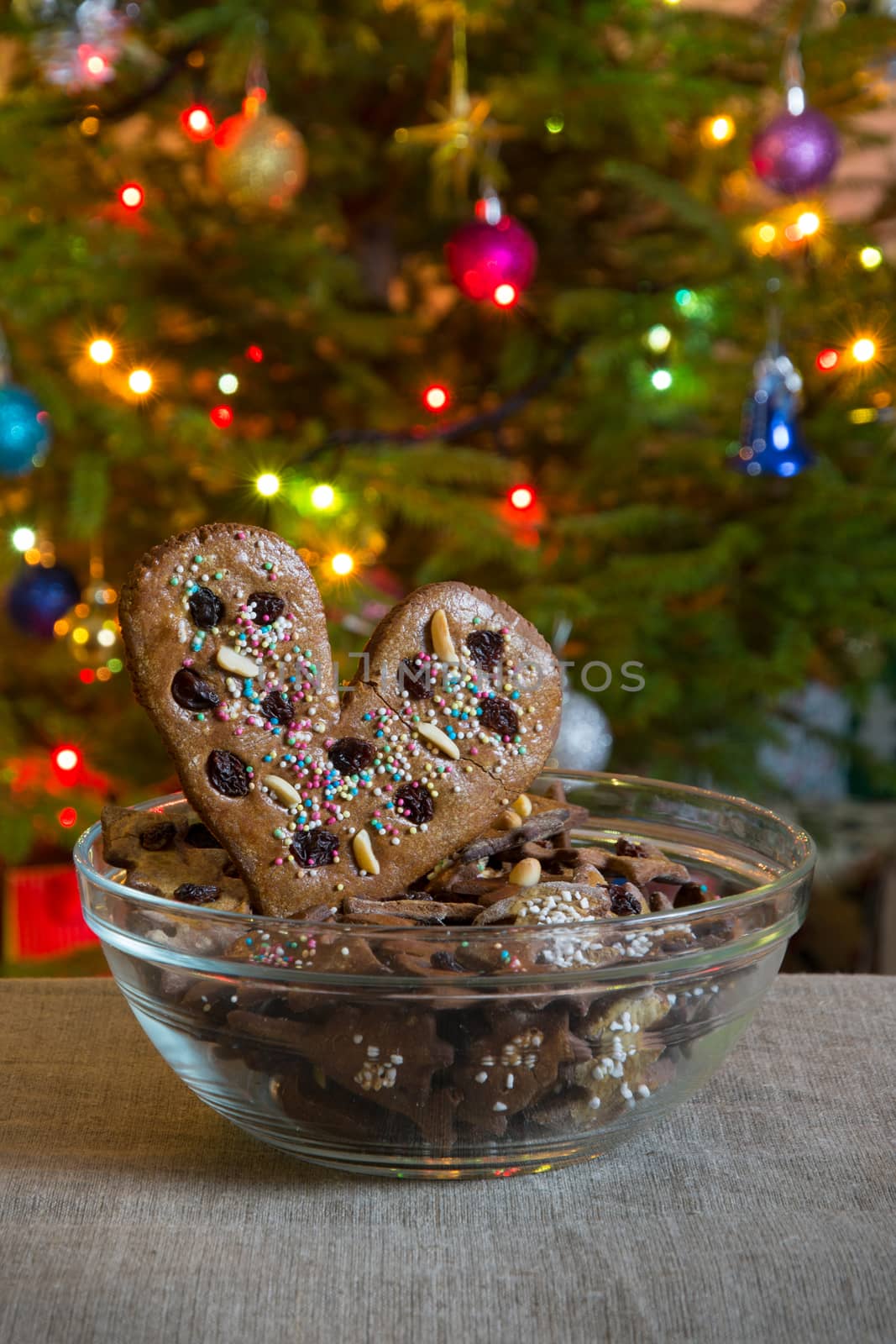 Gingerbread heart, put into glass bowl. Gingerbread heart decorated and Christmas sweets on the background of  decorated Christmas tree.