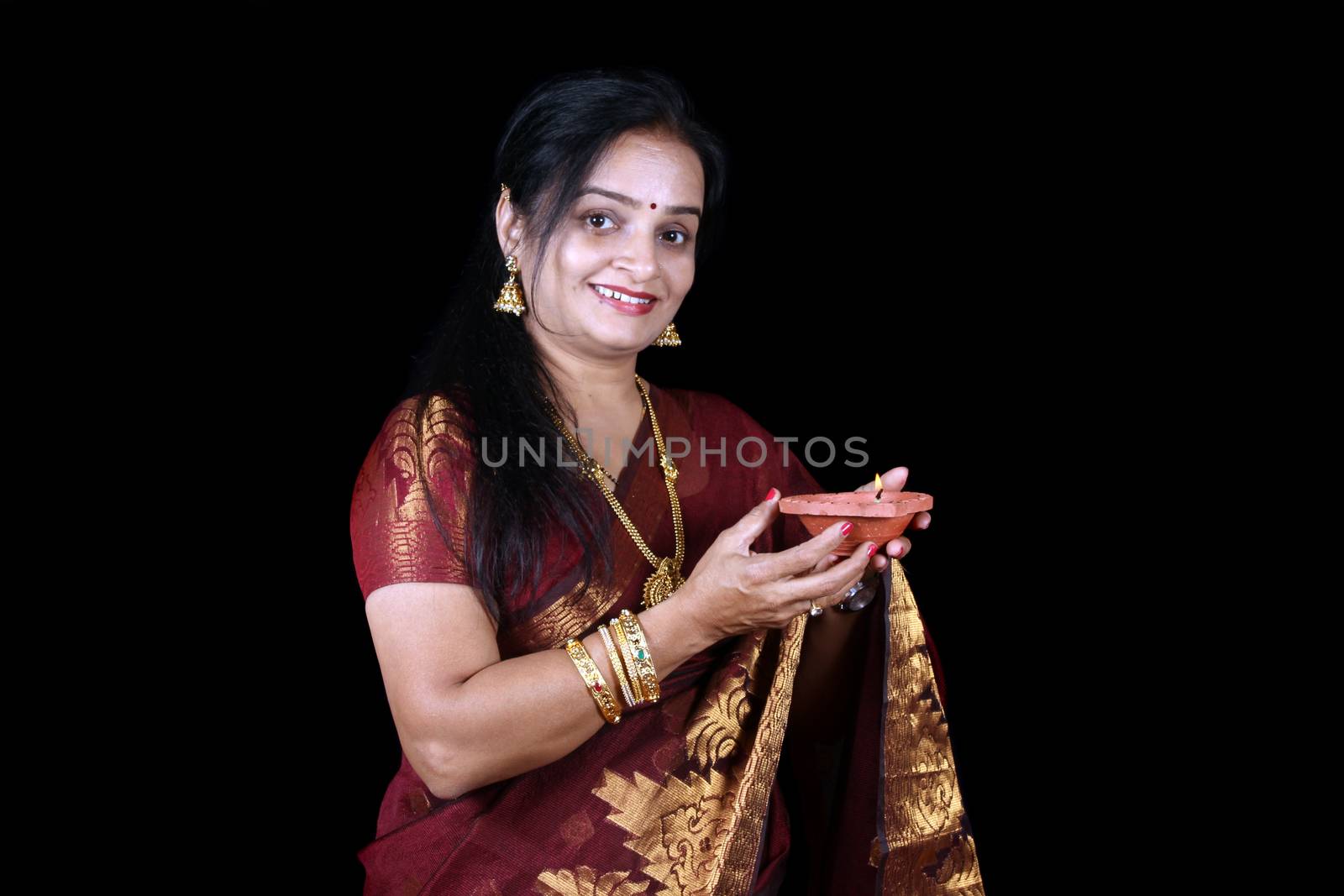 A middleaged Indian woman holding a traditional earthen lamp during Diwali festival in India, on black studio background.