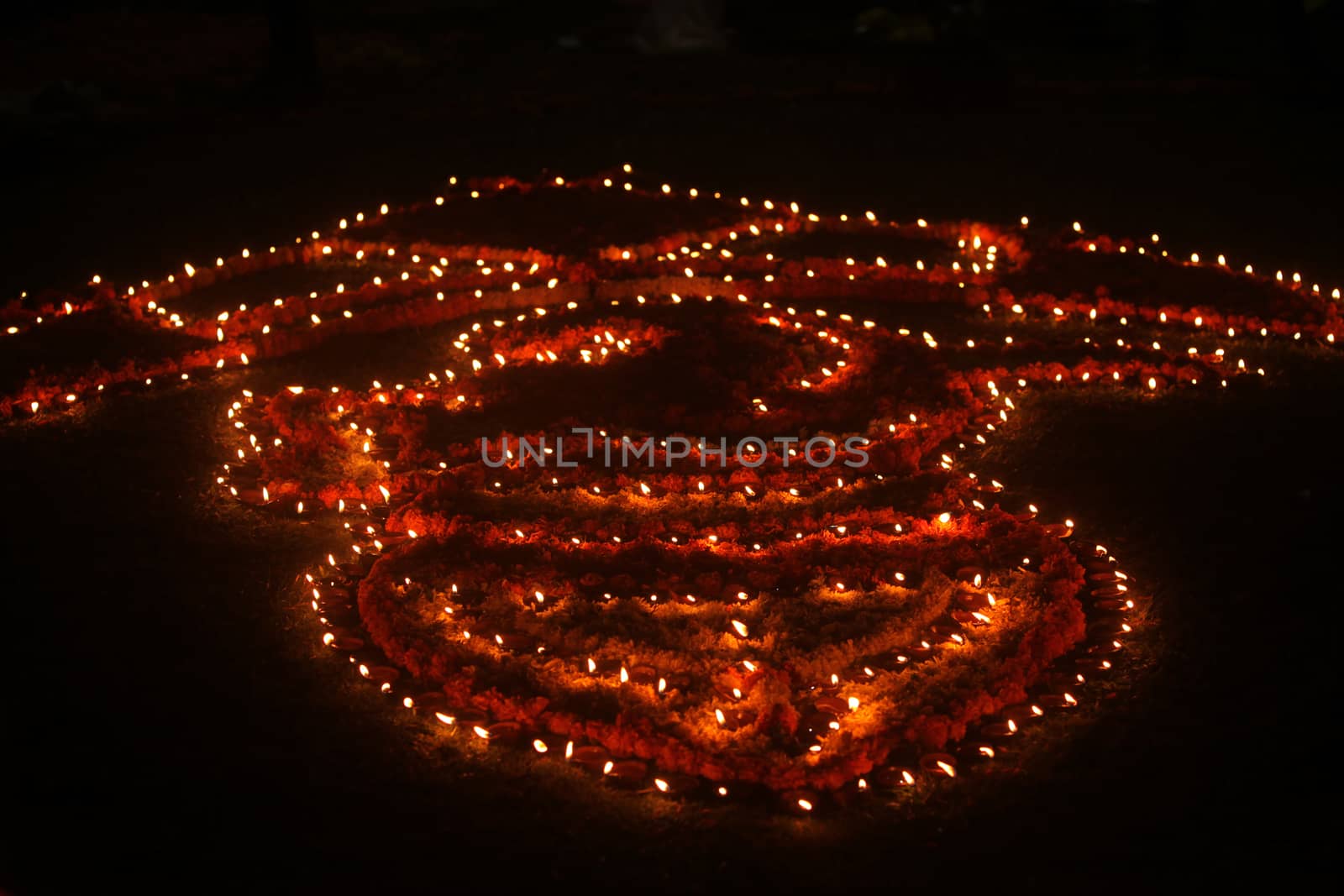 Traditional earthen lamps beautifully setup in a design on a lawn at night, during Diwali festival in India.