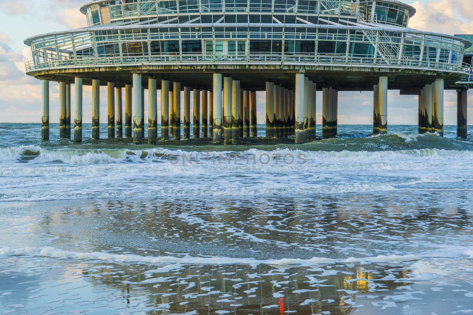 building on stone weathered poles at the beach of scheveningen with waves in the sea and reflection in the wet sand