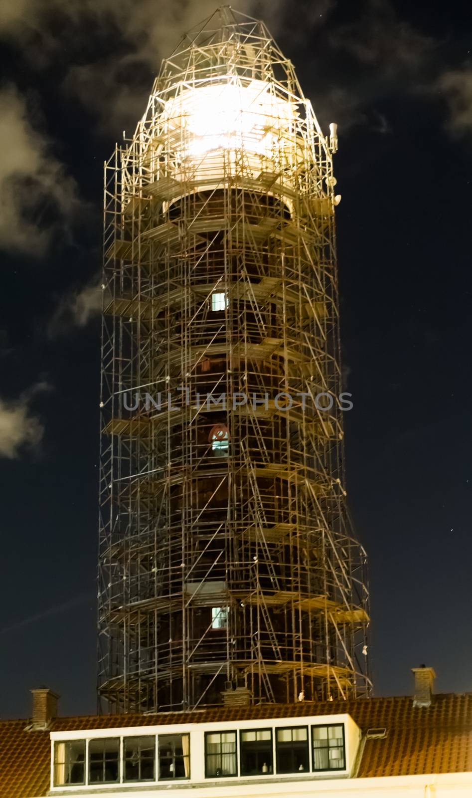 lighthouse in scaffolding for construction with the light shining at night by charlottebleijenberg