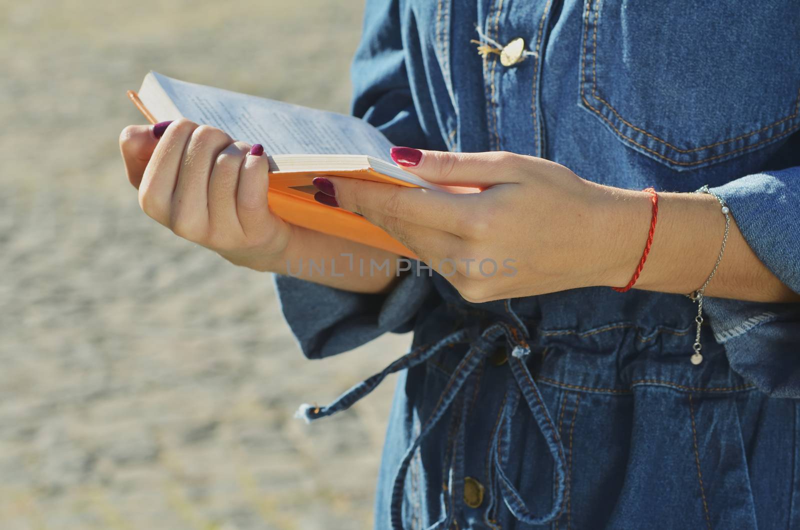 Anonymous young girl wearing a denim jacket holds an open orange book in her hands with a love of reading