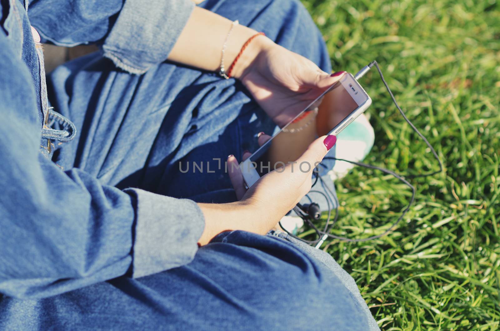 Hands of a young girl who holds a smartphone and sits on the green grass, close-up