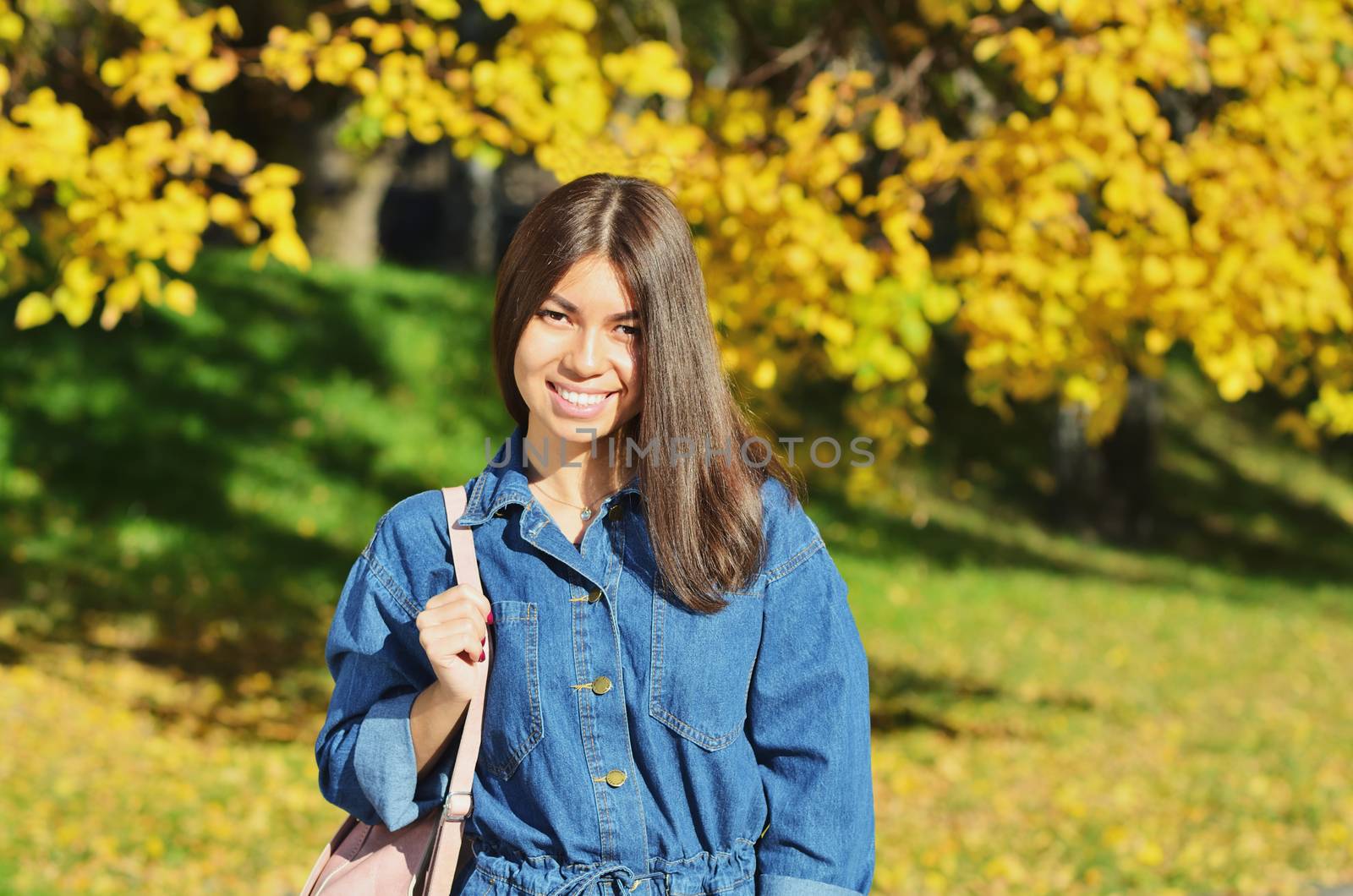 Young happy girl wearing a denim jacket walks through the autumn Park with a backpack