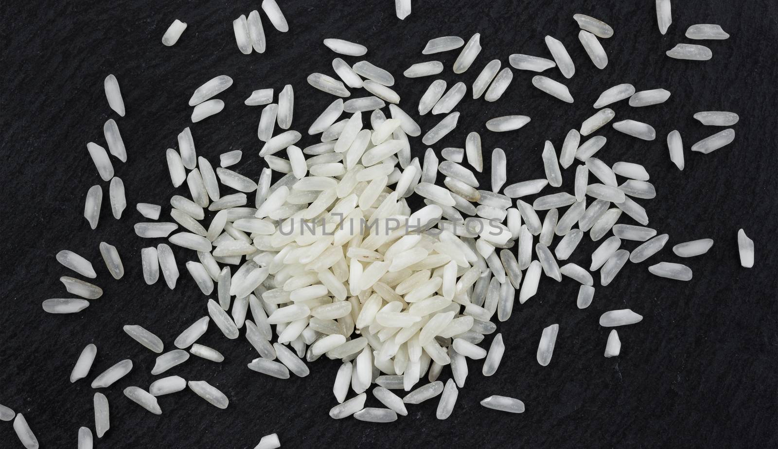 Heap of rice grains on black stone background, top view