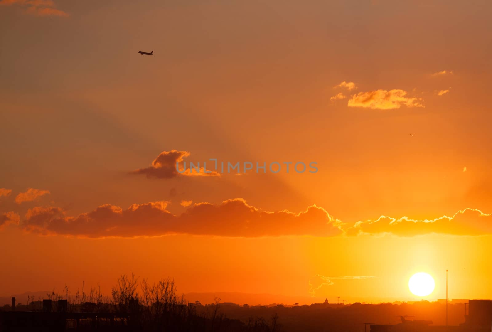 Sun going down on Sydney sending forth its last rays of sunlight as a plane flys off into the distance