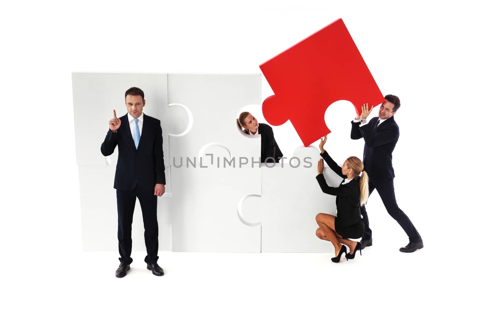 Business team assembling big puzzle and smart businessman standing aside pinting finger up isolated on white background