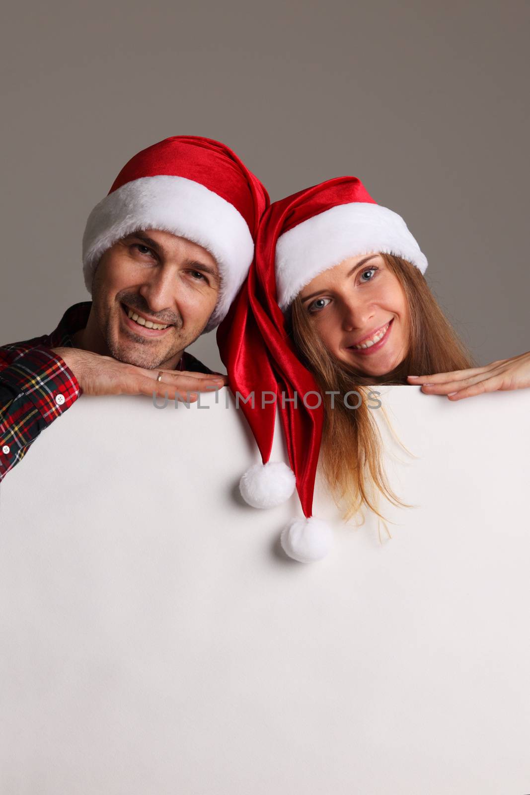 Happy couple in Santa hats holding blank banner with copy space