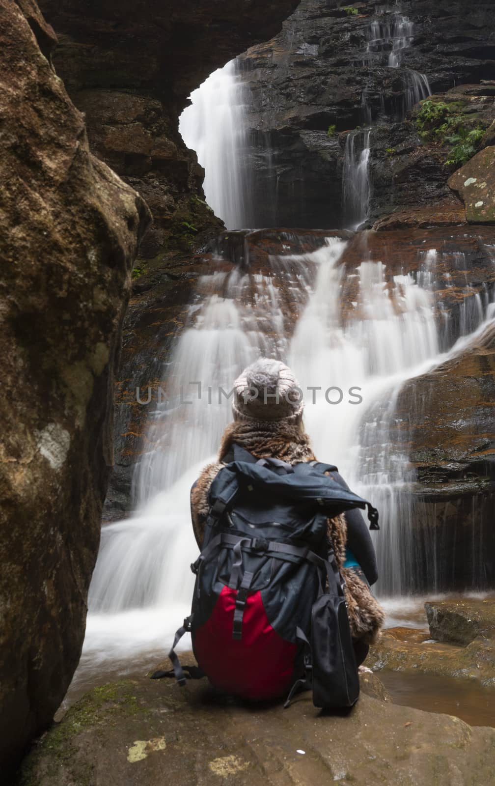 A female bushwalker sitting in awe of the falls watching them flowing freely after rain