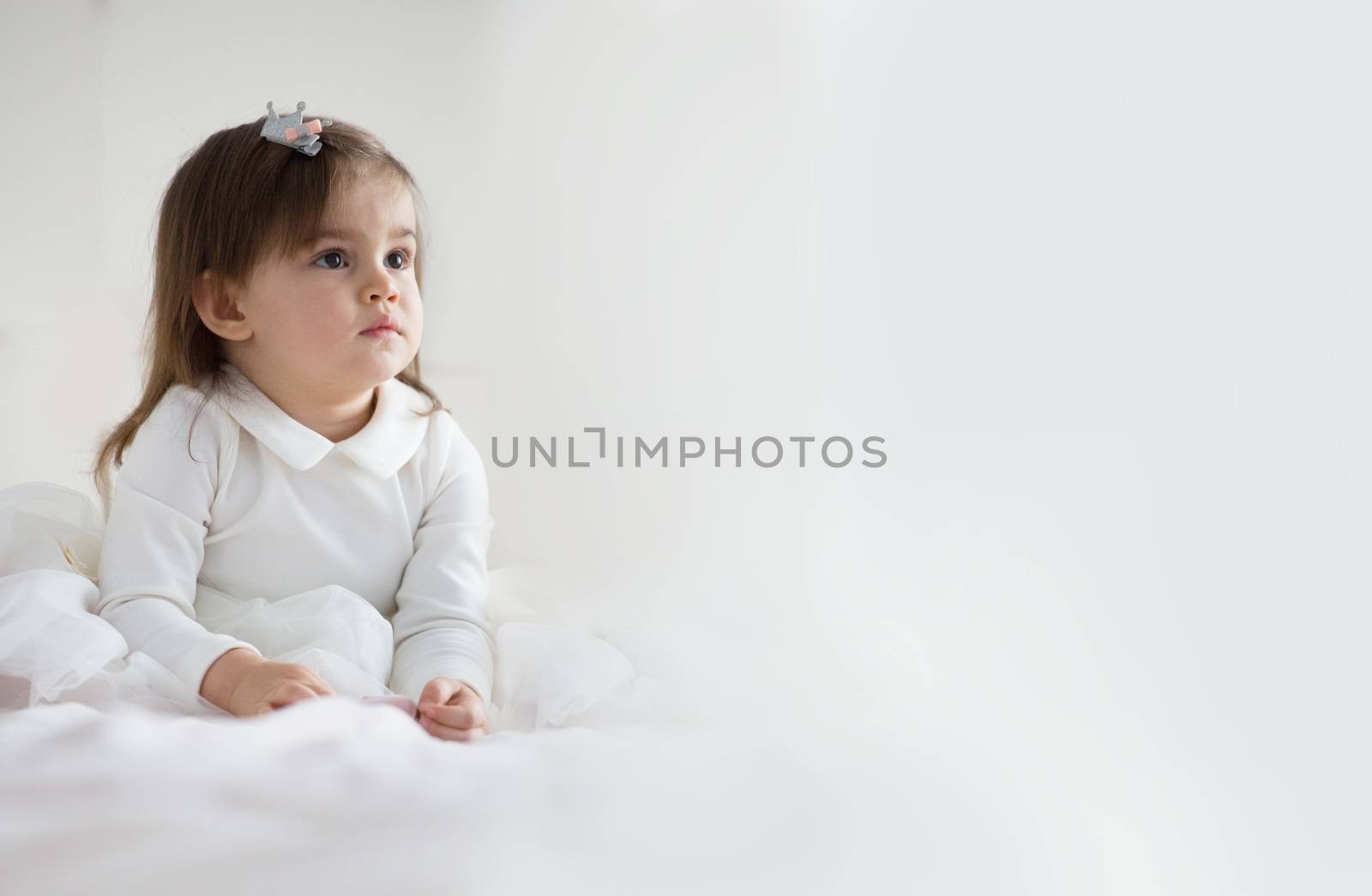 Pretty baby girl with brown hair in white dress over light background with copy space for text
