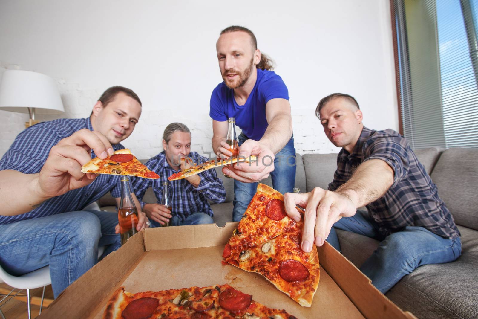 Male friends sitting at home on couch, taking pizza, drinking beer