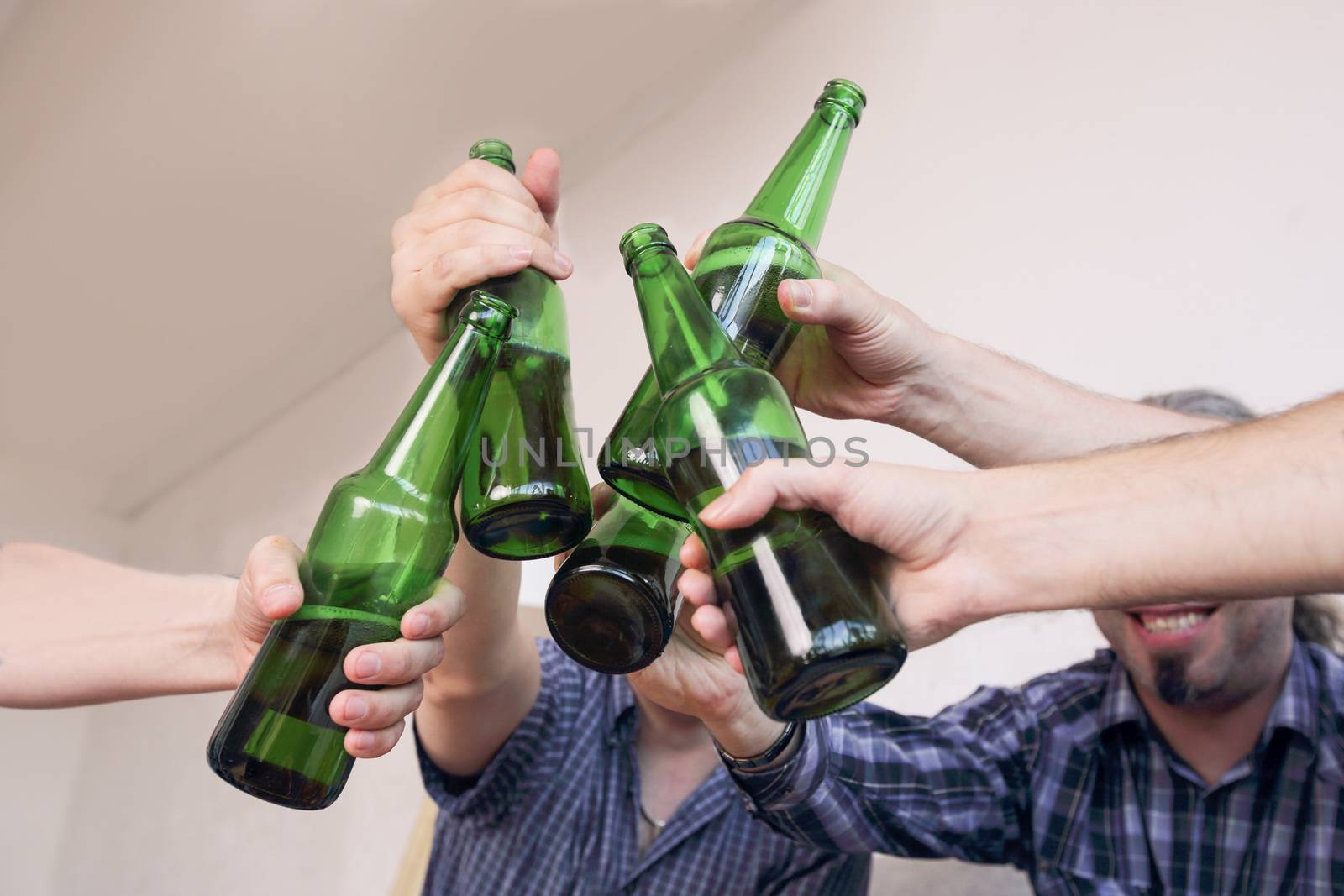 Group of men clinking beer, eating pizza, talking and smiling while resting at home on couch behind TV